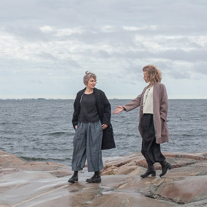 Two people standing on rocks by a body of water with a cloudy sky.
