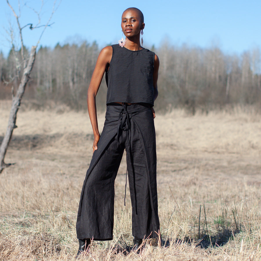A person standing in a field wearing black hemp pants with a wide waist and drawstrings, and a black top.